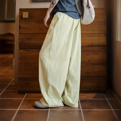 Person wearing light-colored wide-leg pants and a dark top in a room with wooden walls and tiled floor.